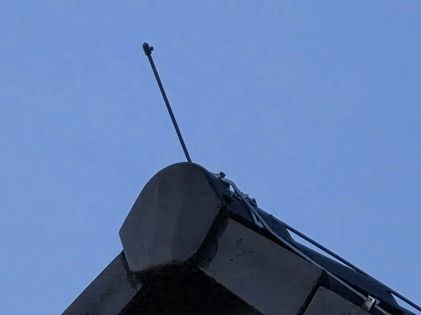 Slim metal air terminal mounted at the gable end of a roof with the roof conductor clipped along the ridge behind it