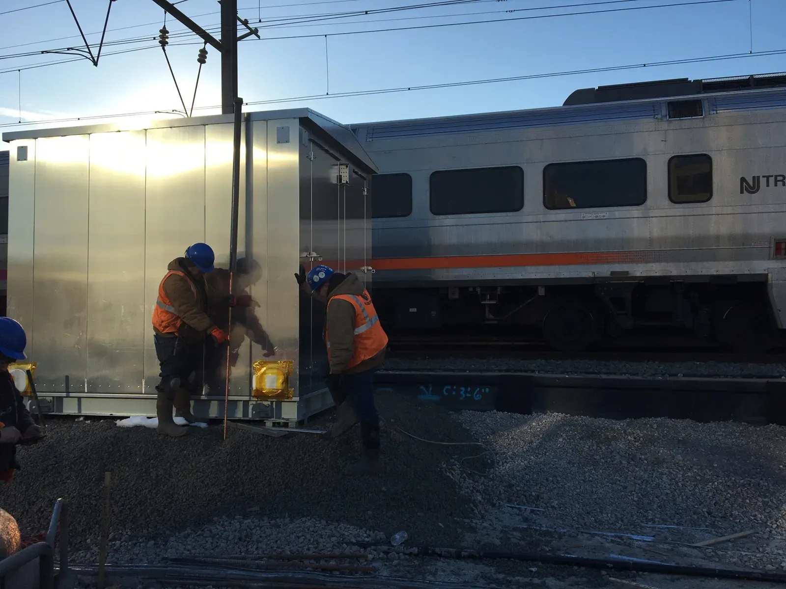 Crew in hi-vis driving grounding rods beside an equipment enclosure