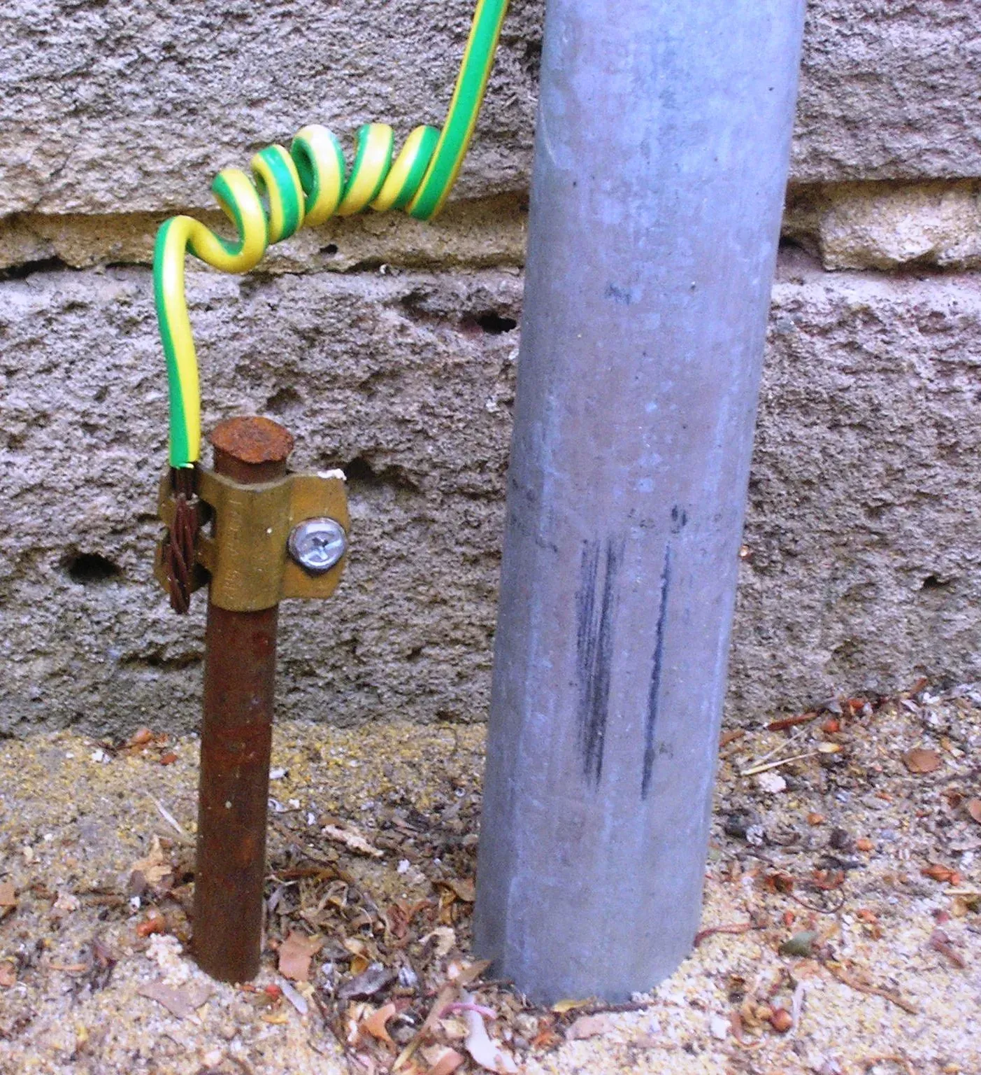 Ground rod with a bolted clamp and green-yellow grounding conductor beside a house wall, the kind of electrode measured by a fall of potential test