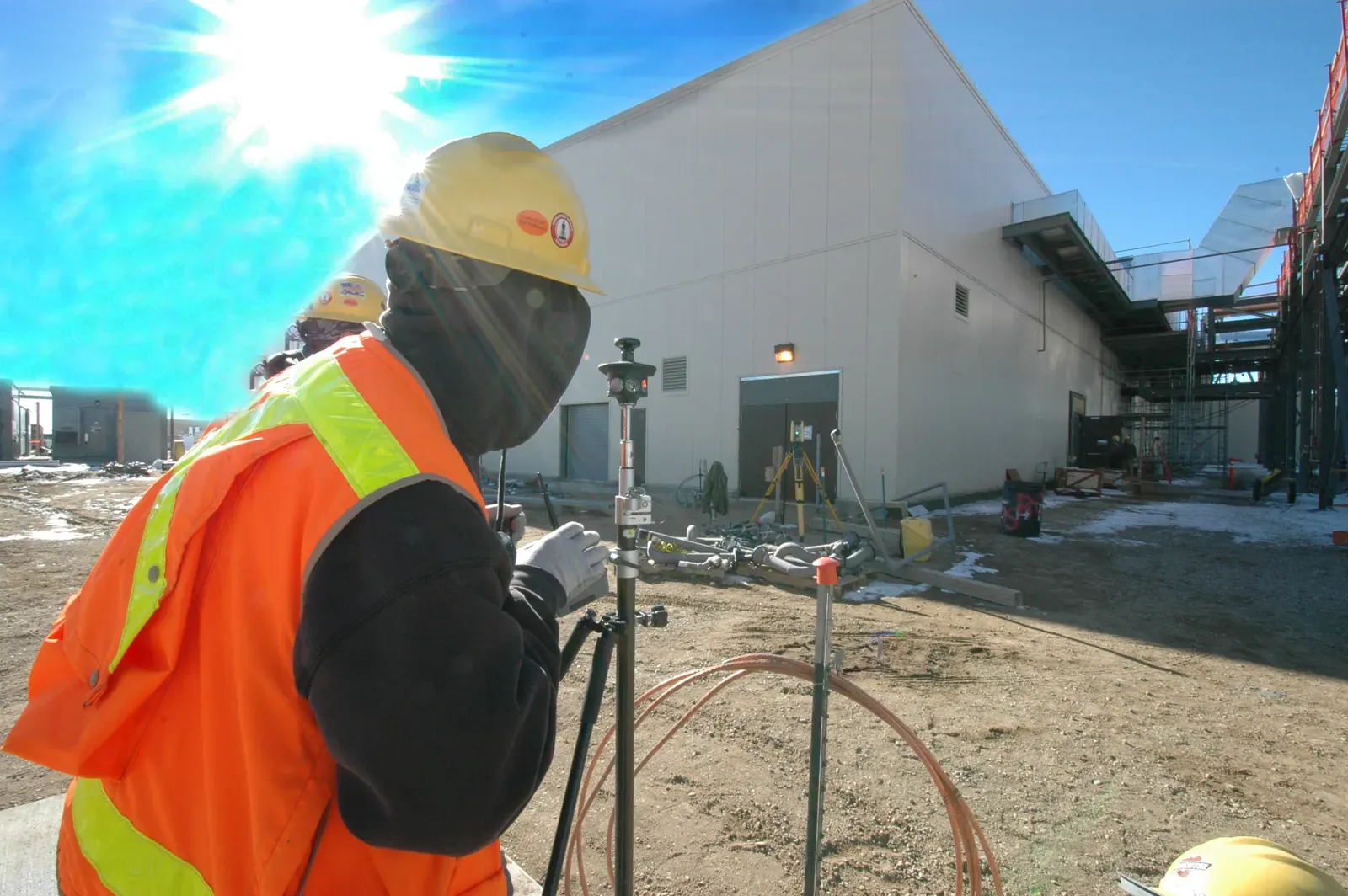Worker in hi-vis beside a high-mast lightning protection pole at an industrial plant