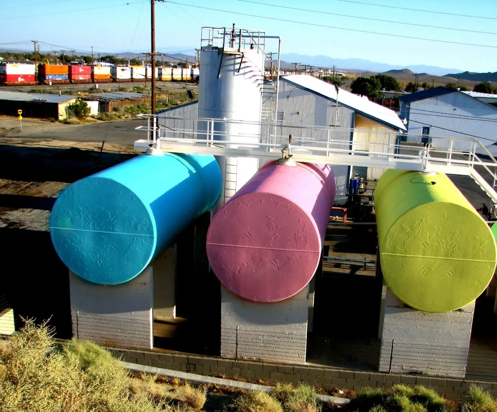Three horizontal steel gasoline storage tanks on concrete saddles with a vertical tank and catwalk behind them