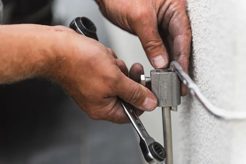 Installer tightening a clamp on a lightning protection down conductor fixed to a wall