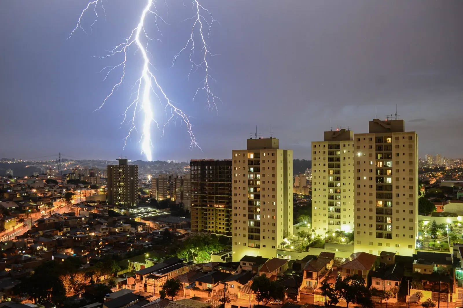 A large lightning bolt over a night skyline of houses and three apartment towers