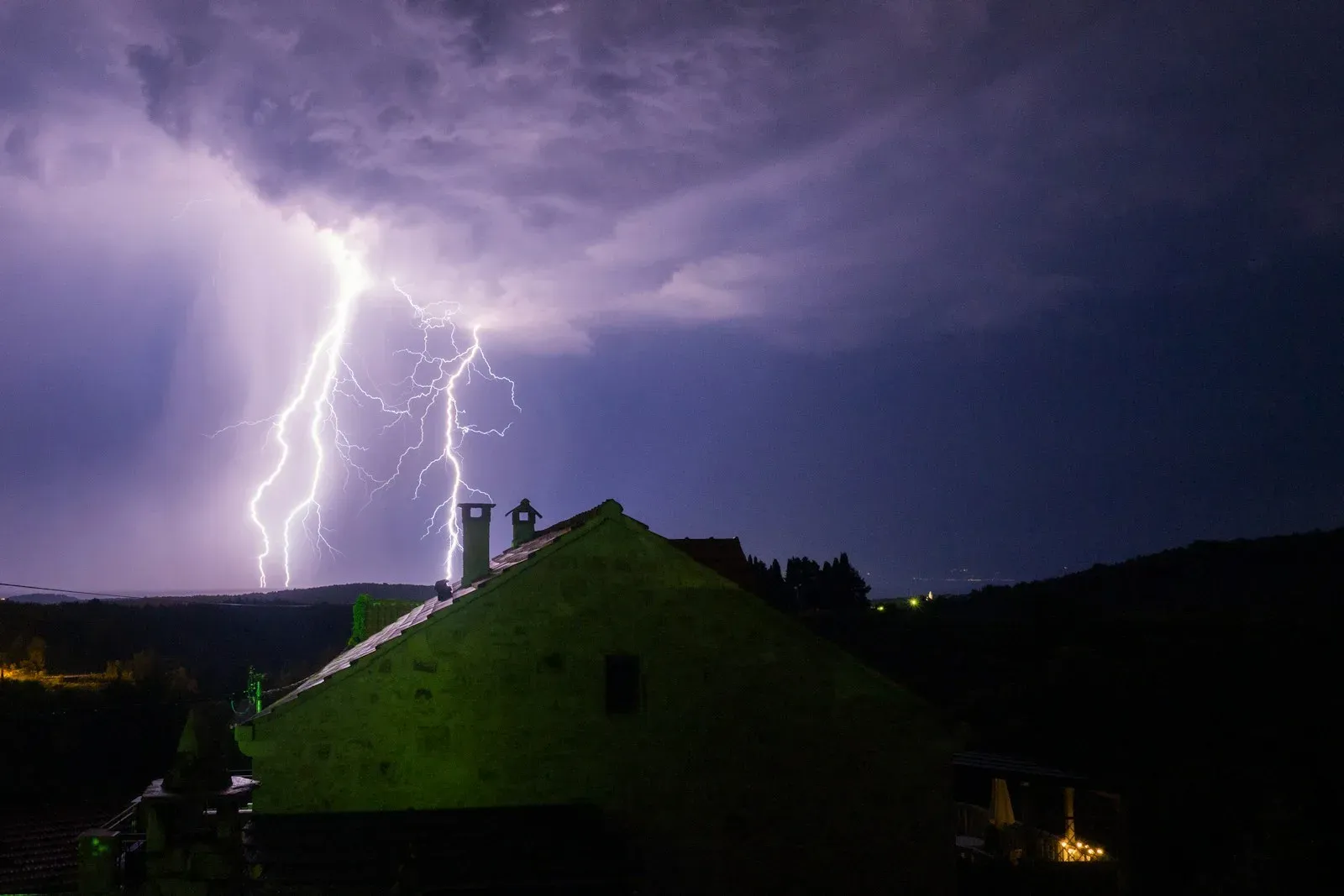 Lightning bolts striking behind a house at night during a summer storm