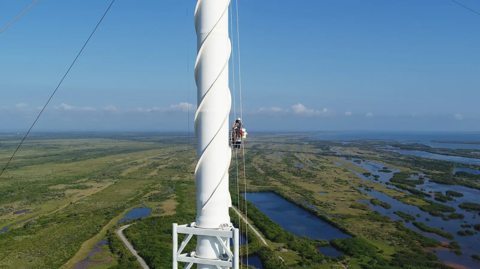 Worker on a rope at the top of a tall white lightning protection tower during maintenance