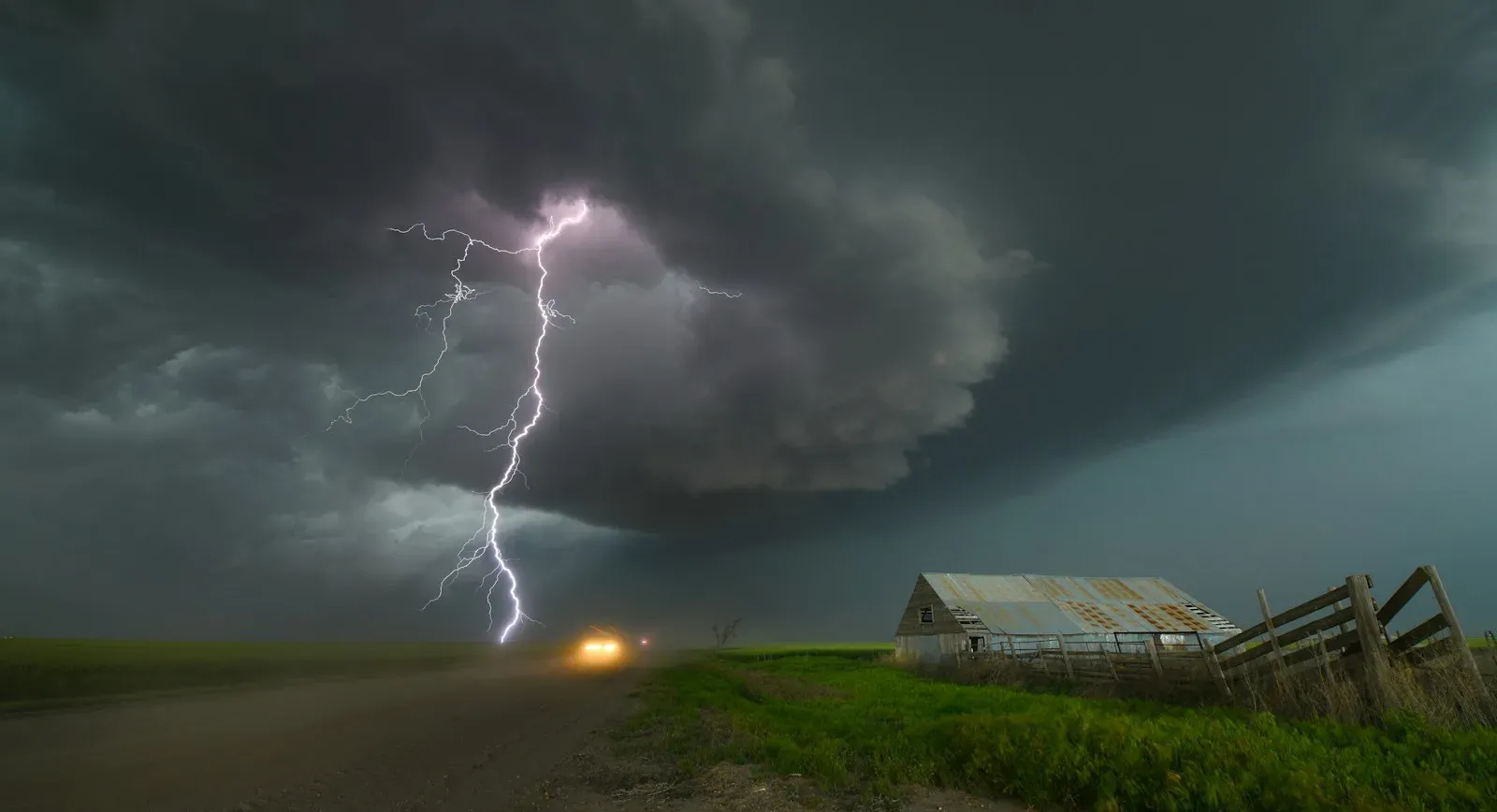 Lightning bolt striking near a rural farm building and road under a dark storm cloud