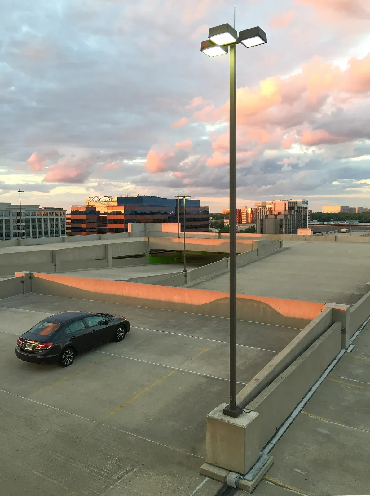 Top level of a concrete parking garage at dusk with a tall light pole topped by an air terminal and the conductor running along the deck