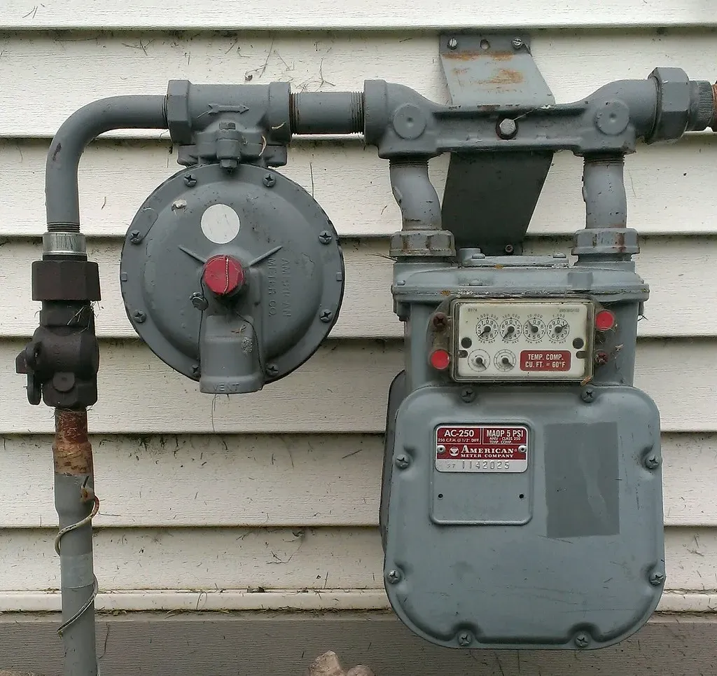 Residential gas meter and regulator on a house wall, with the rigid outlet pipe where a CSST bonding clamp is commonly attached