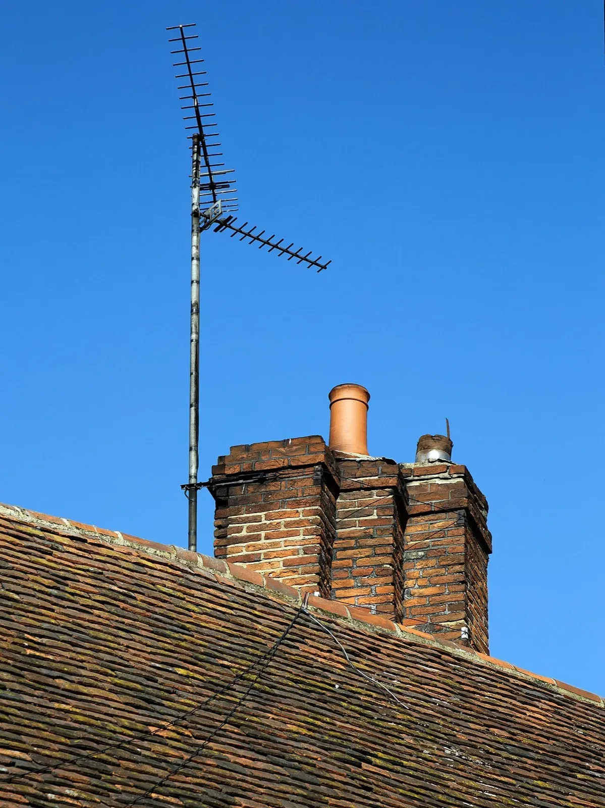 Rooftop TV antenna on a tall metal mast beside a brick chimney on a tile roof