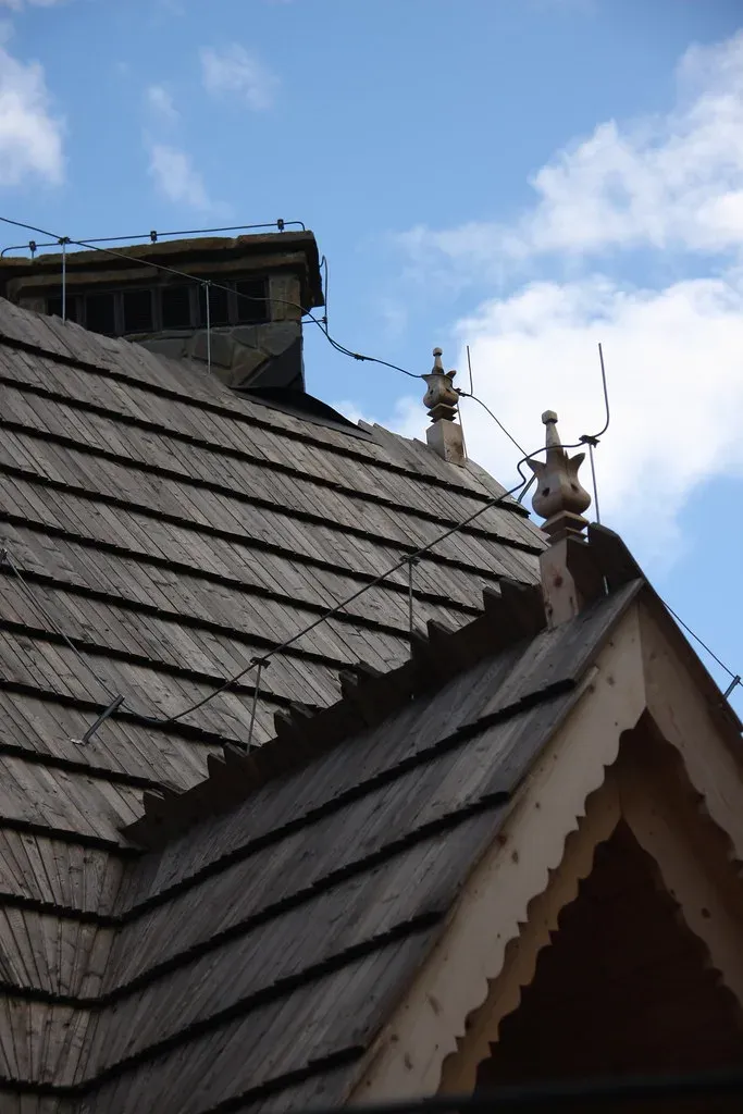 Wooden house roof with lightning rods on the chimney and ridge finials, joined by a conductor clipped along the roof