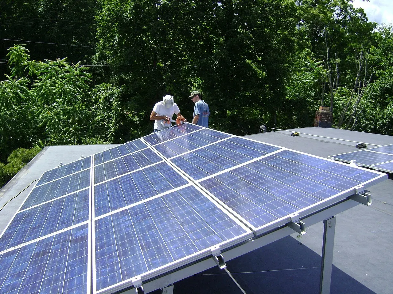 Two workers installing a tilt-up solar panel array on a flat roof near Poughkeepsie, New York